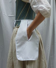 a woman wearing a white dress and holding a white purse in her right hand while standing next to a curtain