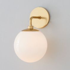 a white ball mounted on the side of a wall light with a gold metal arm