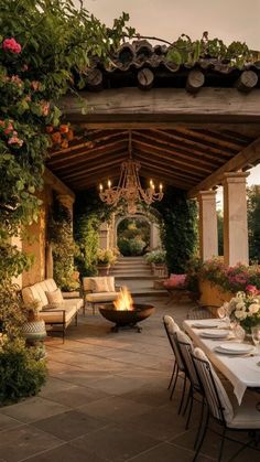 an outdoor dining area with tables and chairs around a fire pit, surrounded by greenery