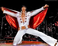 the man is performing on stage with his hands in the air while wearing white and red clothing