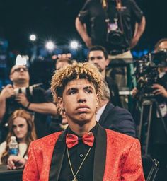 a young man in a red jacket and bow tie is surrounded by photographers at an event