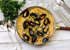 a plate of pasta with mussels and parsley next to silver utensils