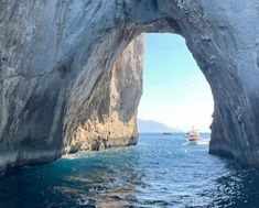 an arch in the side of a rock formation over water with boats floating below it