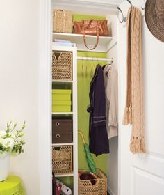 an open closet with baskets and clothes hanging on the wall, next to a green stool