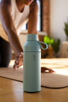 a person bending over with their hands on the floor next to a water bottle and yoga mat