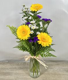 a vase filled with yellow and purple flowers on top of a wooden table next to a white wall