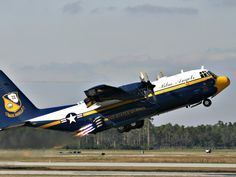 a blue and white airplane taking off from an airport runway with trees in the background