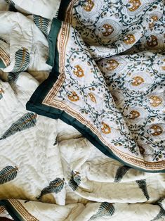 a white and green blanket laying on top of a bed covered in skulls, leaves and flowers