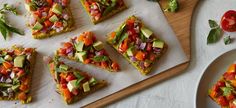 several slices of pizza on a cutting board with tomatoes, avocado and other toppings