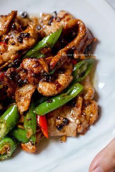 a white plate topped with chicken and green pepper stir - frys on top of rice