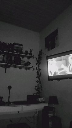 a black and white photo of a living room with a television on the wall, bookshelves in the background