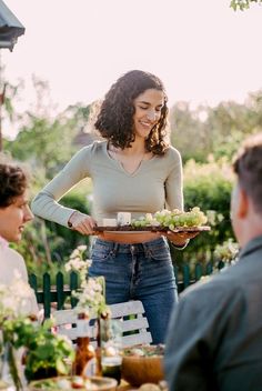 a woman holding a tray full of food while standing next to other people at a table