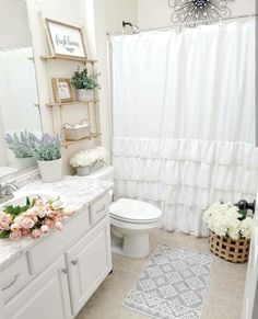 a white bathroom with flowers on the counter and shower curtain over the toilet, along with a rug