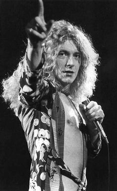 an old photo of a man with long hair holding a microphone and pointing to the side