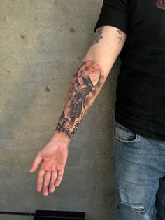 a man with a tattoo on his arm is standing in front of a concrete wall