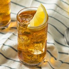 two glasses filled with ice and lemon on top of a striped table cloth next to spoons