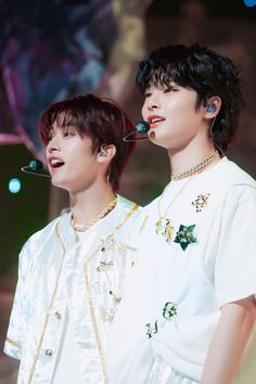 two young men standing next to each other with ear buds in their ears and wearing necklaces