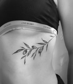 a woman's stomach with an olive branch tattoo on her lower back and the words love secret written across it