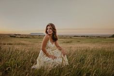 a woman in a dress is sitting in the tall grass with her hands on her hips