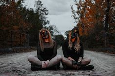 two women wearing masks sitting on the ground