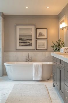 a white bath tub sitting in a bathroom next to two framed pictures on the wall