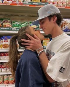 a young man and woman kissing in front of a grocery store shelf with lots of food