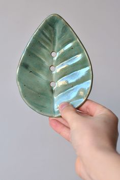 a hand holding a green leaf shaped bowl with two holes in the center and one hole at the bottom