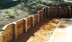 a wooden fence in the middle of a dirt and grass area next to some trees