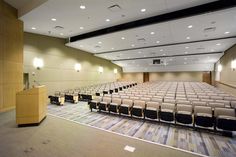 an empty auditorium with rows of chairs and a podium in front of the stage screen