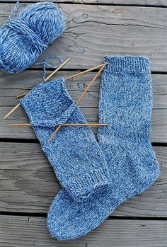 a pair of blue socks sitting on top of a wooden floor next to knitting needles