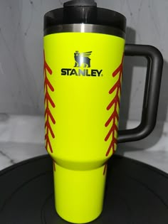 a yellow travel mug with red stitching on the side sitting on a black tray