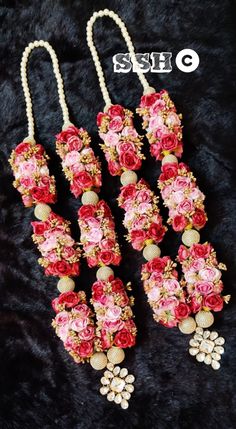 three necklaces with flowers and pearls hanging from them on a black furnishing