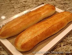 two long loafs of bread sitting on top of a white plate in front of a granite counter