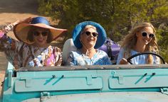 three women in hats and sun glasses riding on a blue vehicle with trees in the background