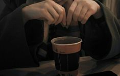 a person sitting at a table with a coffee cup in front of them and their hands resting on the top