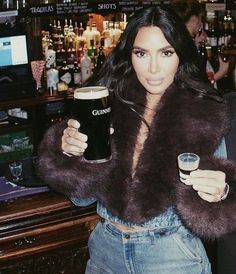 a woman holding a beer in her right hand and wearing a fur coat over her shoulders