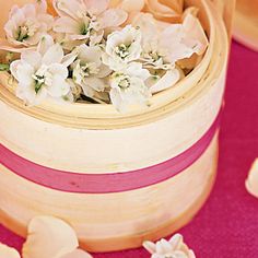 small white flowers in a wooden box on a pink table cloth with petals scattered around it