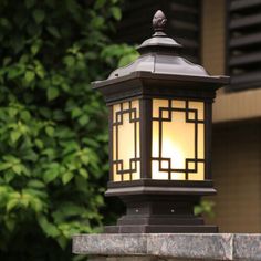 a lamp that is sitting on top of a stone wall next to some bushes and trees