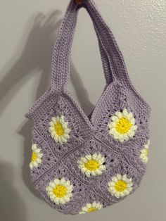 a crocheted purse hanging from a hook on a wall with white and yellow flowers