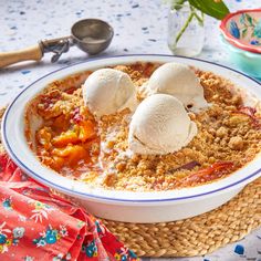 two scoops of ice cream sit on top of a bowl of fruit crumbled