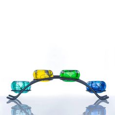 four colorful glasses sitting on top of a metal stand in front of a white wall