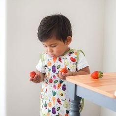 a little boy standing at a table with some food in his hand and looking down