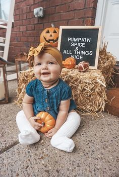 a baby sitting on the ground with pumpkins