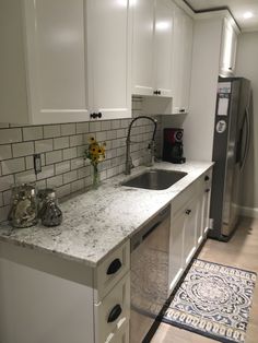 a kitchen with white cabinets and marble counter tops, along with an area rug on the floor