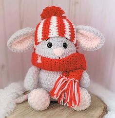 a crocheted stuffed animal wearing a red and white scarf sitting on top of a piece of wood