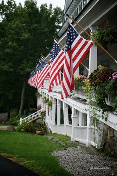 several american flags are hanging on the side of a house in front of some flowers