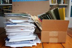 a cardboard box filled with files next to a pile of papers on a wooden floor