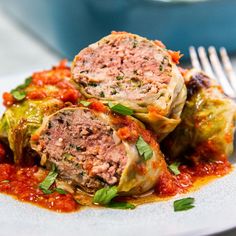 three stuffed cabbages with meat and sauce on a white plate next to a fork