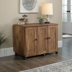 a wooden cabinet sitting on top of a hard wood floor next to a lamp and potted plant