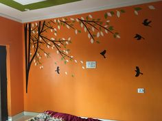 an orange bedroom with birds painted on the wall and tree decal above bedding